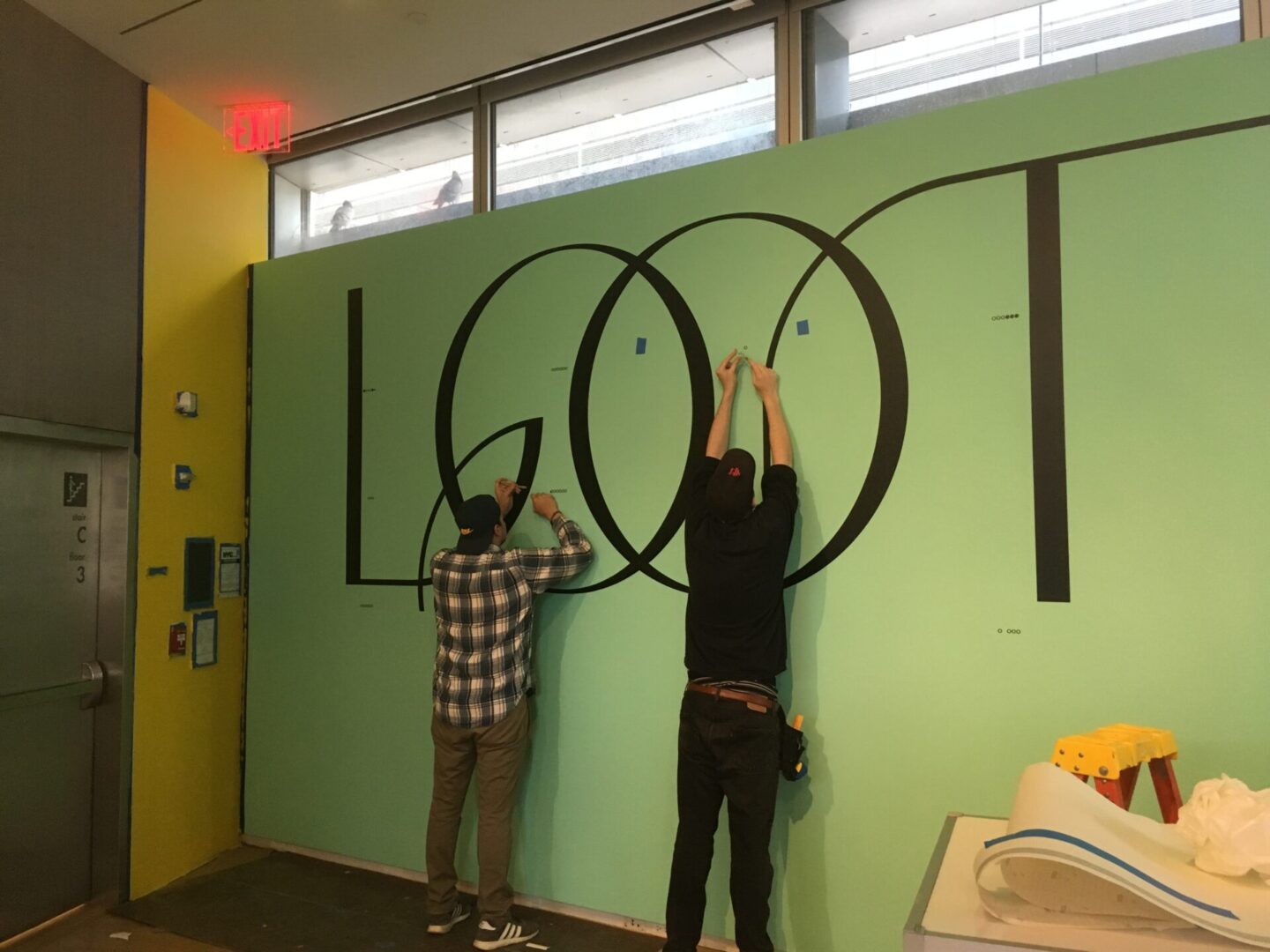 Two men are painting a wall with letters.